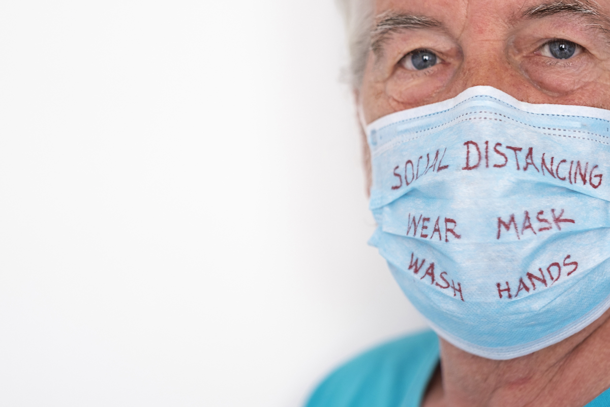 Coronavirus. Serious senior man wearing protective mask with text to avoid coronavirus infection, on white background. Closeup on face with blue eyes